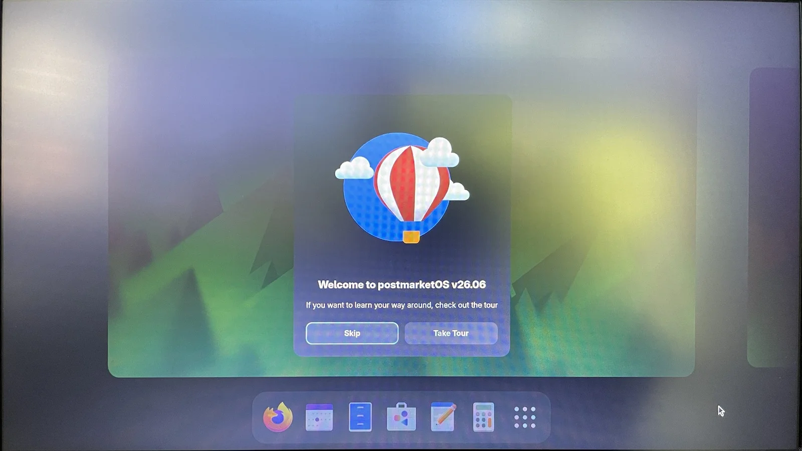 A GNOME desktop with a welcome card reading Welcome to postmarketOS v26.06, a hot air balloon illustration, and a dock with Firefox, Calendar, Files, Software, Text Editor and Calculator
